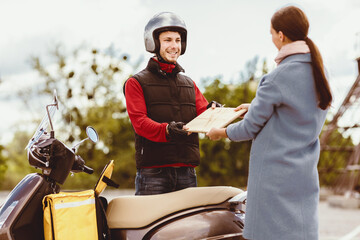 Naklejka premium Delivery Concept. Courier Giving Paper Package To Woman Delivering Documents And Restaurant Meals On Scooter Outside. Selective Focus