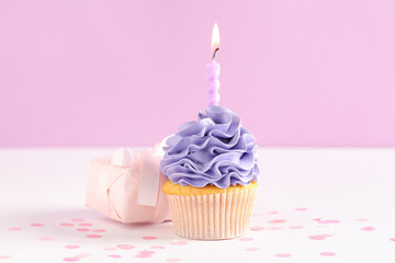 Sweet Birthday cupcake with burning candle and gift box on white table