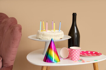 Birthday cake with party hat and cups on table in messy room