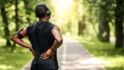 Fototapeta premium African guy sportsman rubbing his injured back, exercising at summer park, back view, empty space