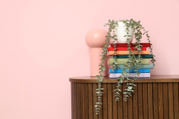 Stacks of books and houseplant on wooden cabinet near pink wall
