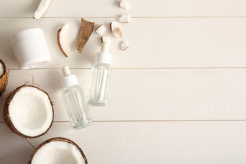 Bottles of coconut cosmetic oil and jar with cream on white wooden background