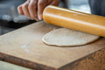 A person is rolling out dough on a wooden board