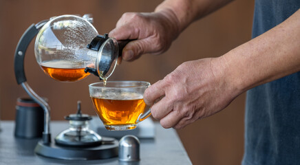 A man is pouring tea into a cup from a glass pitcher
