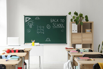 Interior of empty classroom with school desks and text BACK TO SCHOOL on chalkboard