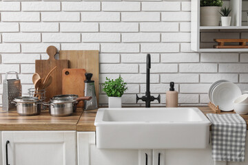 Wooden kitchen counter with clean dishes and ceramic sink near light brick wall