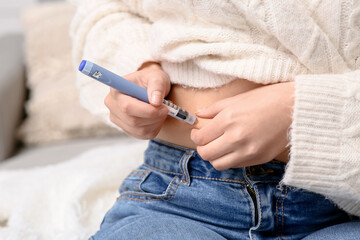 Young woman with diabetes giving herself insulin injection at home, closeup