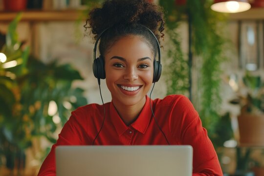Female boss with wired headphones headset talking remotely with colleagues, using laptop for video call, businesswoman in red shirt smiling satisfied inside office at workplace