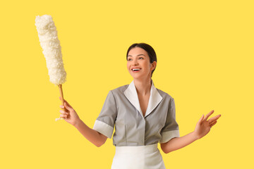 Beautiful young chambermaid with pp-duster on yellow background
