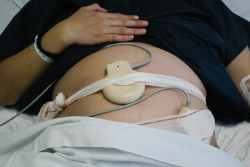 Pregnant woman wearing fetal monitoring device in hospital bed