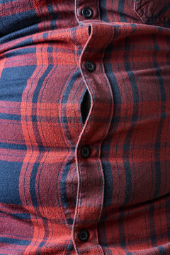 Close up of strained buttons on plaid shirt over man's belly