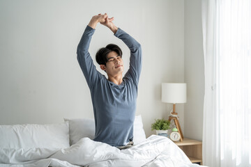 Asian young handsome man getting up from sleep on bed in the morning. 