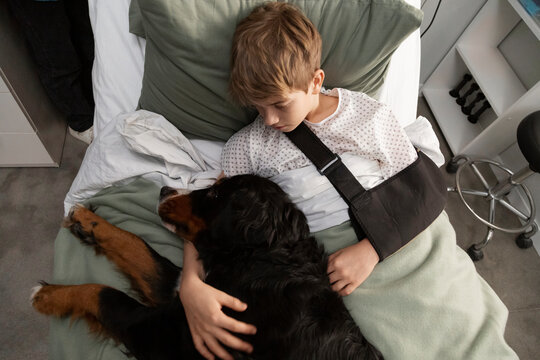 Injured child with arm sling embraces bernese mountain dog 