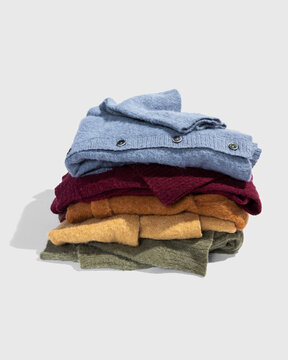 A stack of loosely folded sweaters on a light grey table top.
