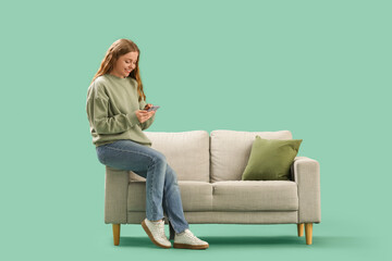 Obraz premium Beautiful young woman with mobile phone sitting on stylish grey sofa against green background