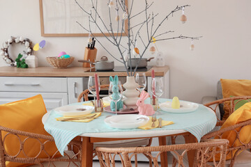 Beautiful Easter table setting with rabbits and tree branches in kitchen