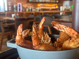 A bowl of deep-fried shrimp served in a rustic setting. The golden-brown crust gives a crispy texture to the fresh seafood.