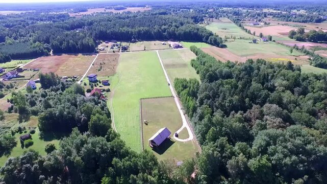 Daugava aerial panoramic view with a wide-angle lens, showcasing patchwork fields, dense green forests, scattered houses, and a building casting a long shadow, under a bright blue sky