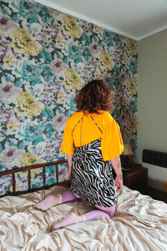 Woman kneeling on bed with floral wallpaper in background
