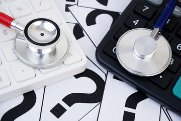 Choosing medical clinic and hospital concept. Cost of medical treatment. Two different stethoscopes on question marks and calculators.