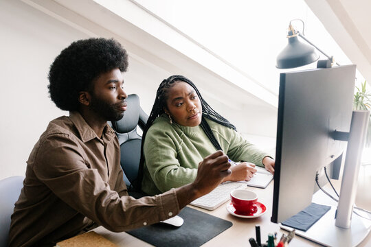 Two coworkers seated at a table in an office setting, working together - Powered by Adobe
