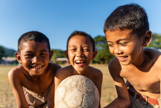 Three cheerful boys with a football in rural Thailand