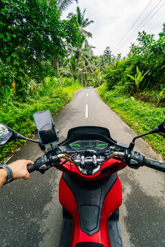 Tourist riding red scooter exploring Bali tropical rainforest road