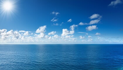bright blue sky over calm ocean with fluffy white clouds and sunlight