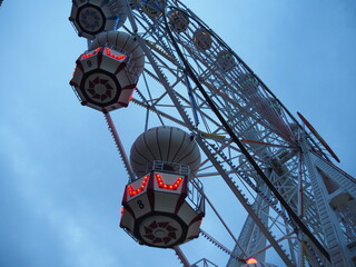 A Ferris wheel in Turkey with lit-up gondolas at dusk, against a cloudy sky.