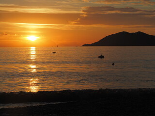 Obraz premium A golden sunset over the sea in Turkey, with a dark silhouette of a hill and gentle waves on the shore.