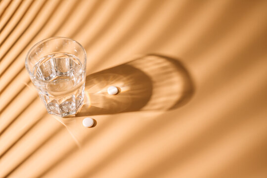 Medicine pills and cup of water at beige background. 