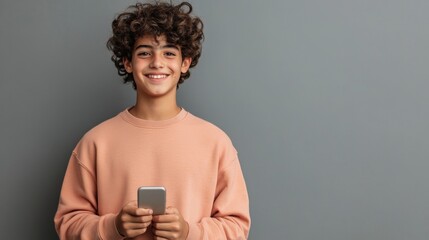 Teen with curly hair holding a smartphone smiles against a gray background