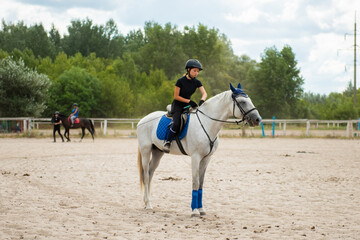 Training process. Young teenage girl jockey wearing helmet riding horse on sand arena practicing in...