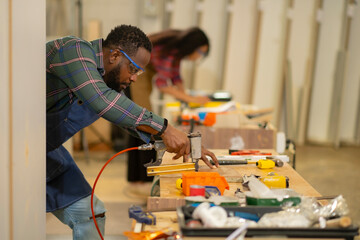 Fototapeta premium African American man and woman do thire work at furniture factory happily and professtionally, carpenter occupation, labor job holliday., using equipment for work.
