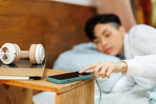 Young woman in cozy bedroom stopping phone alarm from bed
