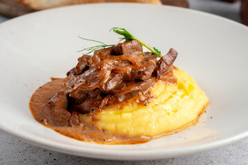 Stewed chicken liver with mashed potatoes and onions served on a white plate. Close-up