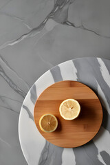 Gray marble background and marble table surface, on the table is a wooden kitchen board on which a lemon is neatly cut.