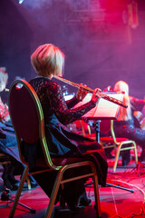 Woman playing the flute. Concert of the symphony orchestra under bright scenic spotlights.