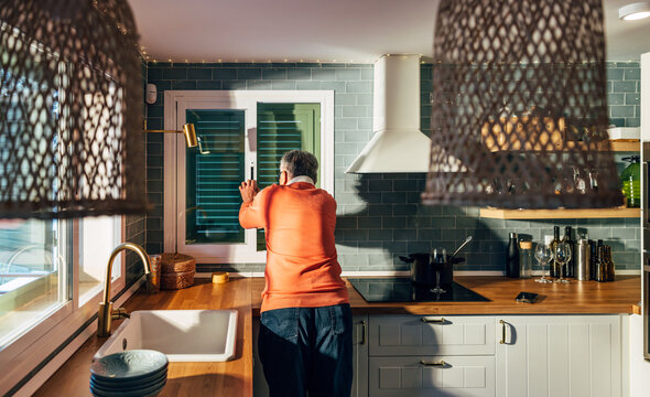 Man in cozy kitchen looking out window at morning light