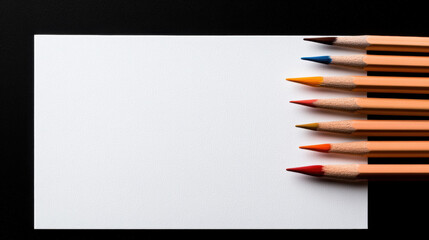 Obraz premium A blank white paper positioned next to colorful pencils on a simple desk for creative brainstorming sessions
