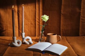 candle composition with one flower and natural textiles, cup, book