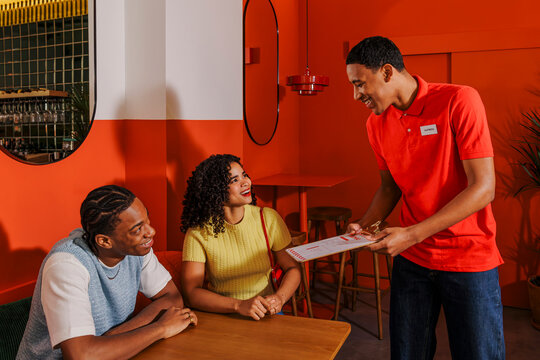 Smiling waiter showing menu to young couple in a restaurant