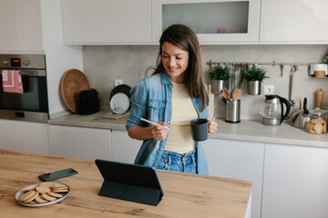 Smiling Woman Enjoying Coffee While Watching Tablet in Modern Kitchen