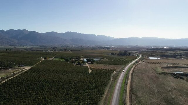 Aerial: Transport truck drives highway past fruit orchards, mtn plateau