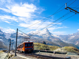 Gornergrat Bahn, red tourist train going up to the Gornergrat train station near Zermatt with amazing view, Matterhorn peak, blue sky background, famous tourist destination do not miss at Switzerland.
