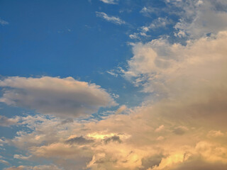 A captivating skyscape filled with fluffy clouds. Some clouds are white, while others are illuminated with a warm, golden sunlight, creating a beautiful contrast against the blue sky.