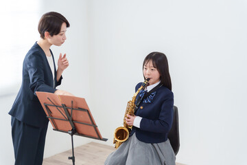 サックスを吹くブラスバンド部員と顧問の女性教師