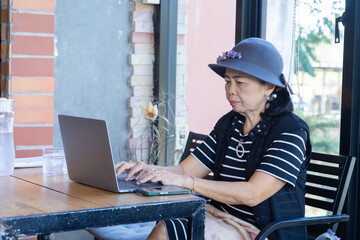 Lifestyle elderly female after retirement checking stock investment performance in digital tecnology laptop at cafe talk to friends using smartphone, healthy lifestyle pensioner drink wine on holiday
