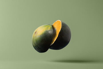 Watermelon cut in half revealing orange inside on pastel green background, creative food fusion...
