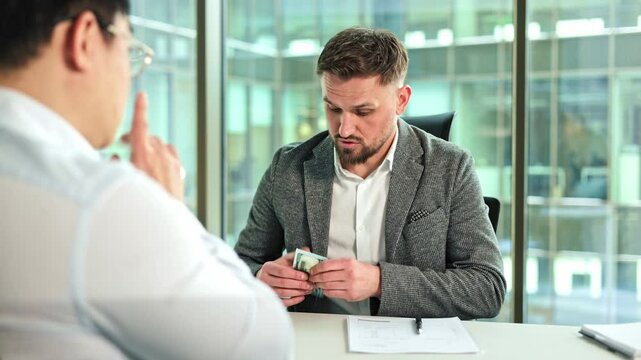 Two businessmen discuss a contract. One businessman puts money into the inside pocket of his jacket. They shake hands and continue talking.